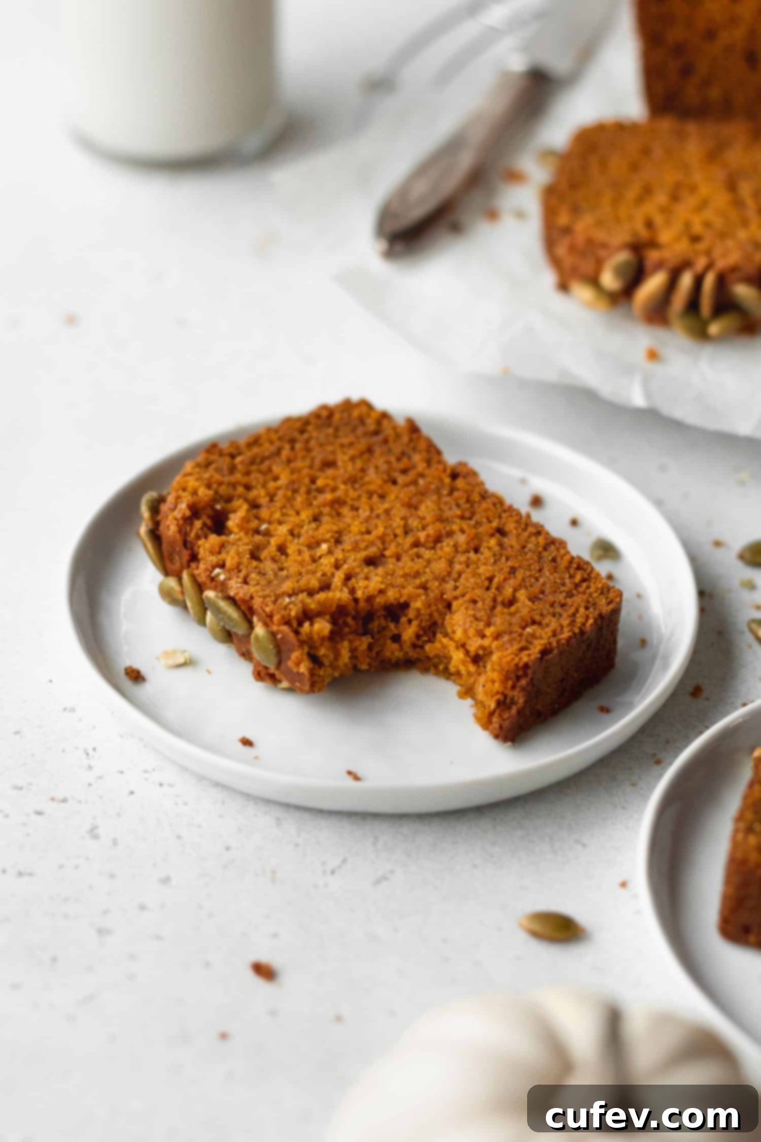 A close-up of a bitten slice of moist gluten-free pumpkin bread on a plate, showing the soft interior.