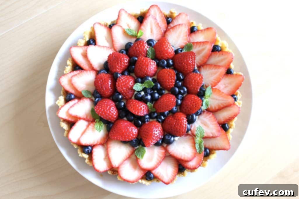 Vibrant strawberry and blueberry tart, garnished with fresh mint, showcasing its refreshing appeal