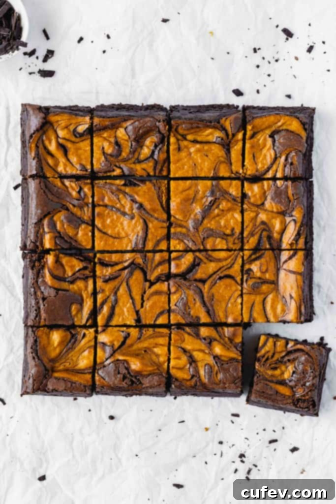 Pumpkin cheesecake brownies cut into squares on parchment paper.