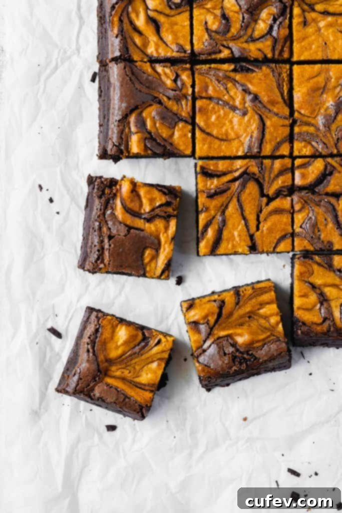 Three pieces of pumpkin cheesecake brownies scattered next to more brownies on a piece of parchment paper.