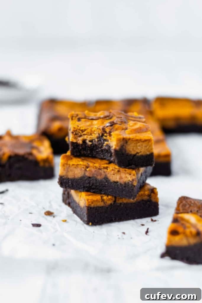 A stack of three pumpkin cheesecake brownies with more brownies scattered around.