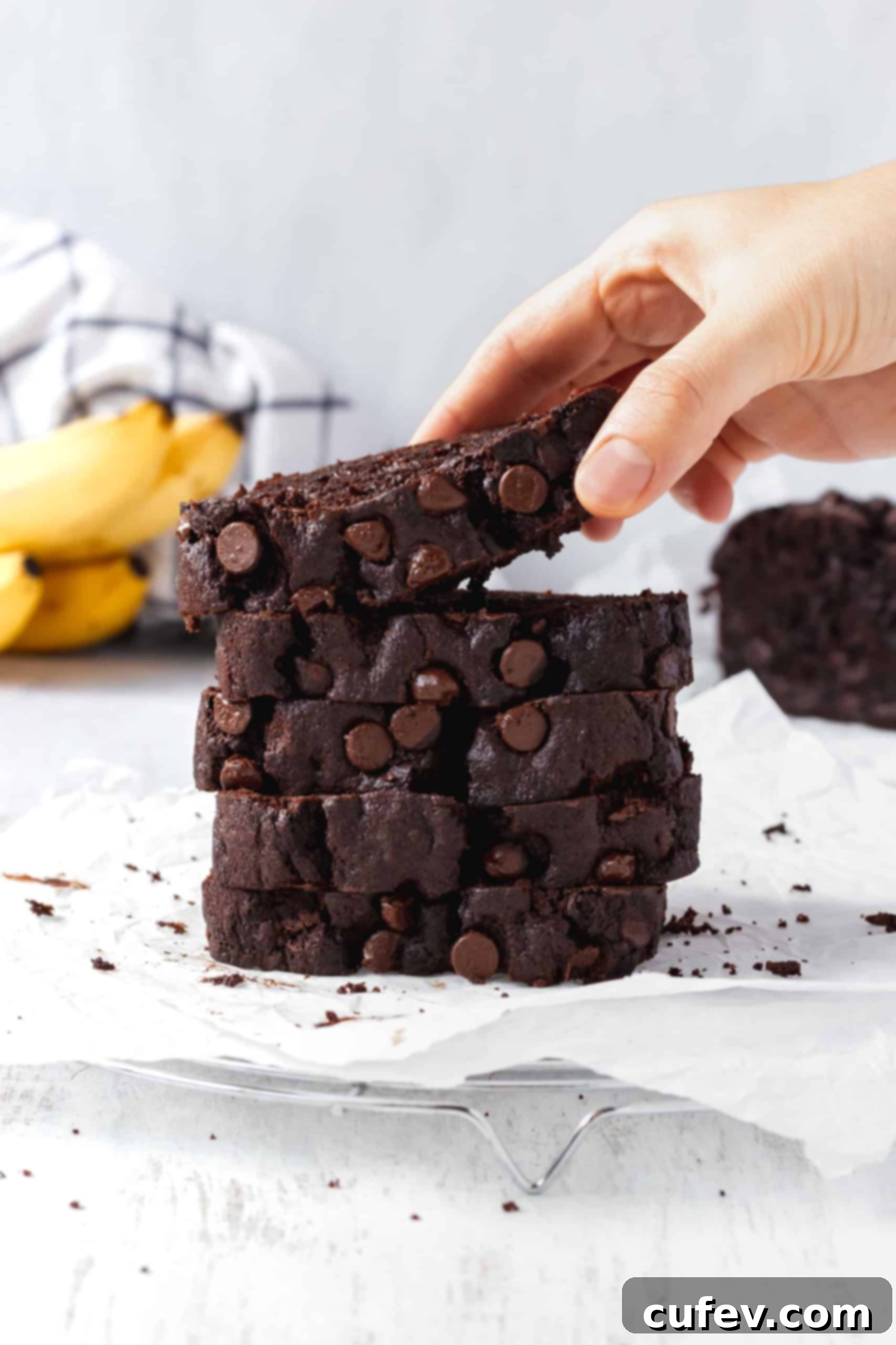 Chocolate Banana Bliss 2 A stack of chocolate banana bread with a hand picking up a slice, showcasing its moist texture and abundant chocolate chips.