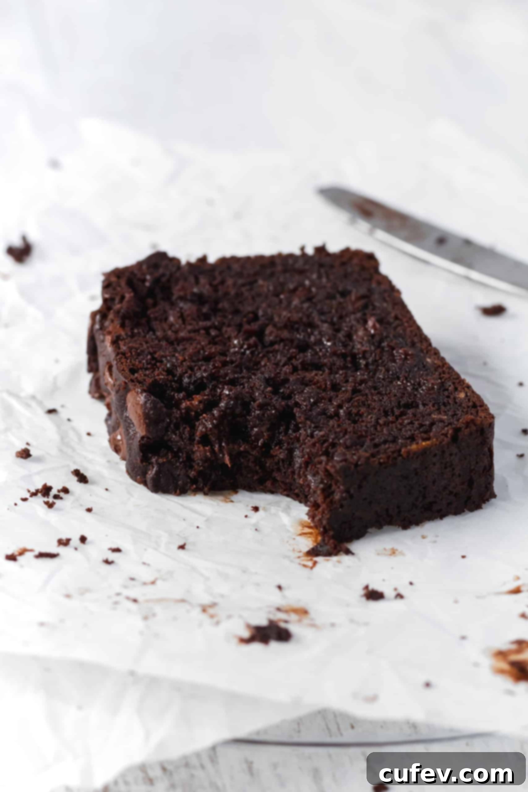 Chocolate Banana Bliss 4 A bitten slice of moist chocolate banana bread on parchment paper with chocolate stains, emphasizing its richness.