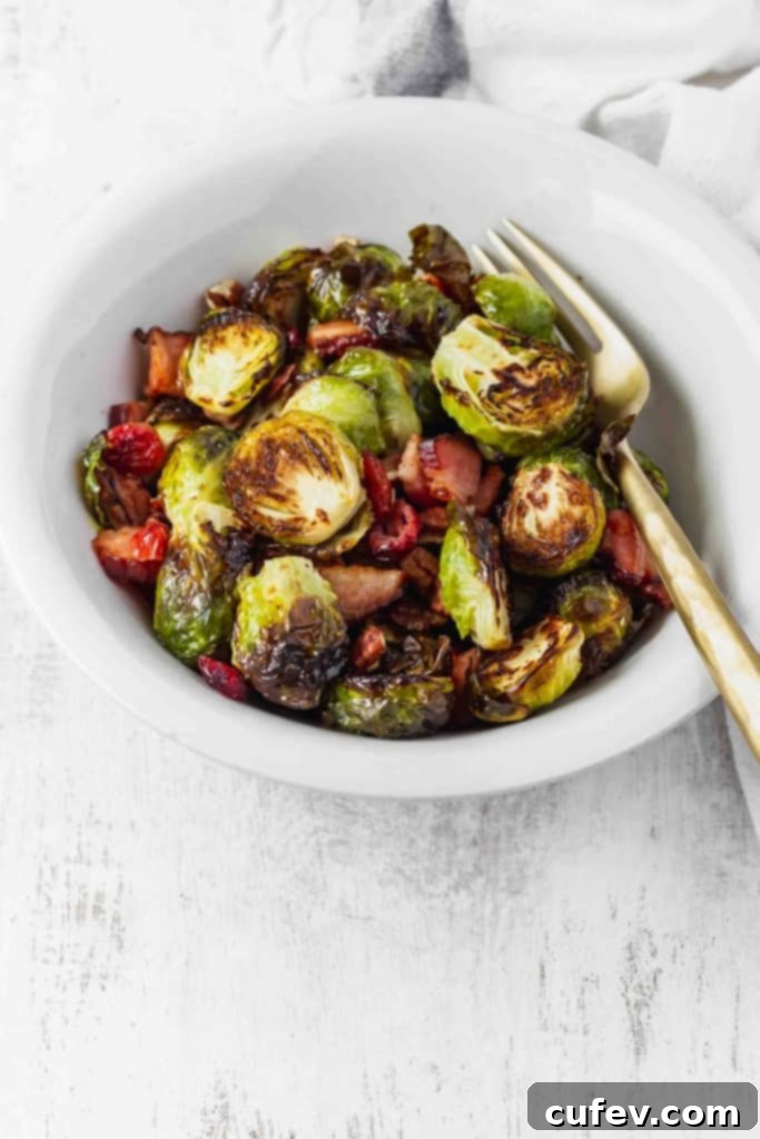 Preparing Brussels sprouts for roasting with bacon, cranberries, and pecans on a baking sheet.