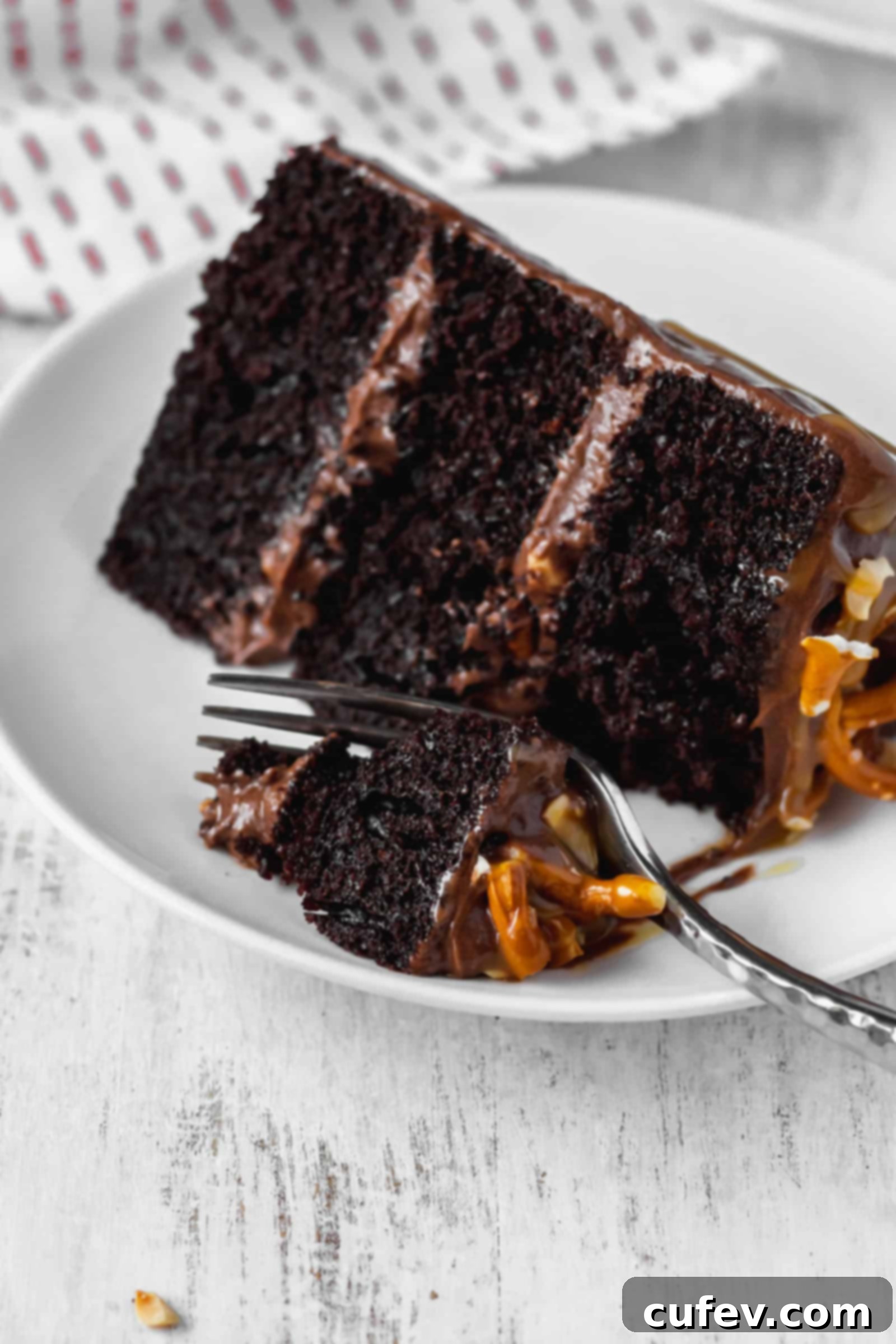 A fork cutting a bite out of a slice of moist chocolate cake with peanuts and pretzels, showing texture