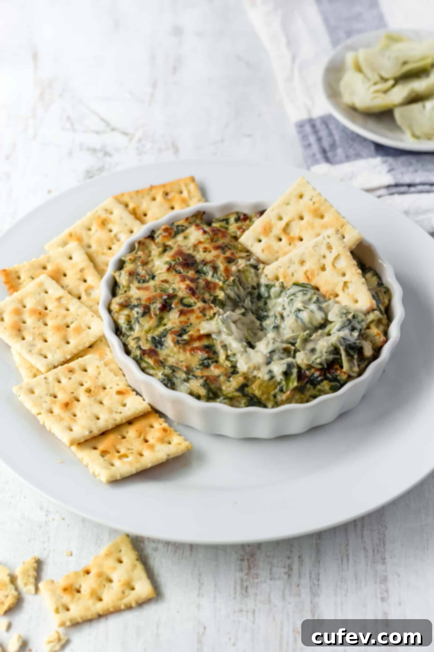 Close-up of two crackers dipped into a rich, hot vegan spinach artichoke dip, showing its inviting texture.