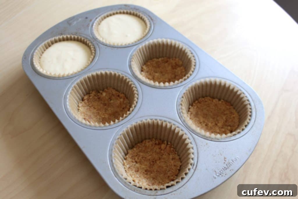 Raw cheesecake batter poured into cupcake liners with crusts, ready for baking