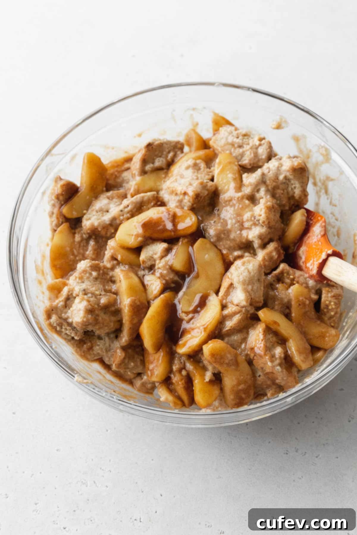 Cozy Vegan Bread Bake 13 A vibrant close-up showing the rich, spiced apple pie filling being gently folded into the soaked cubes of bread and vegan custard in a mixing bowl.