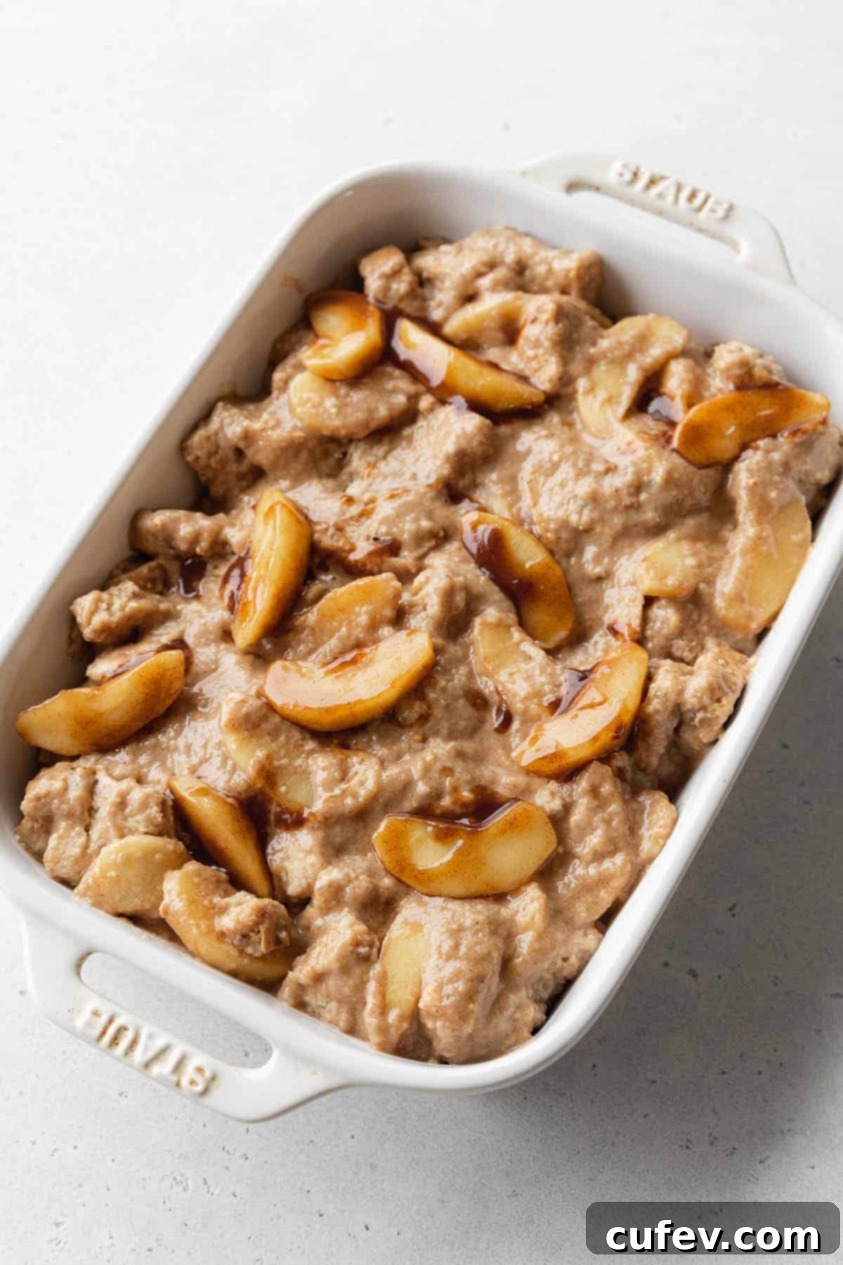 Cozy Vegan Bread Bake 14 A white casserole dish filled with the uncooked vegan apple pie bread pudding mixture, ready to be placed into the oven.