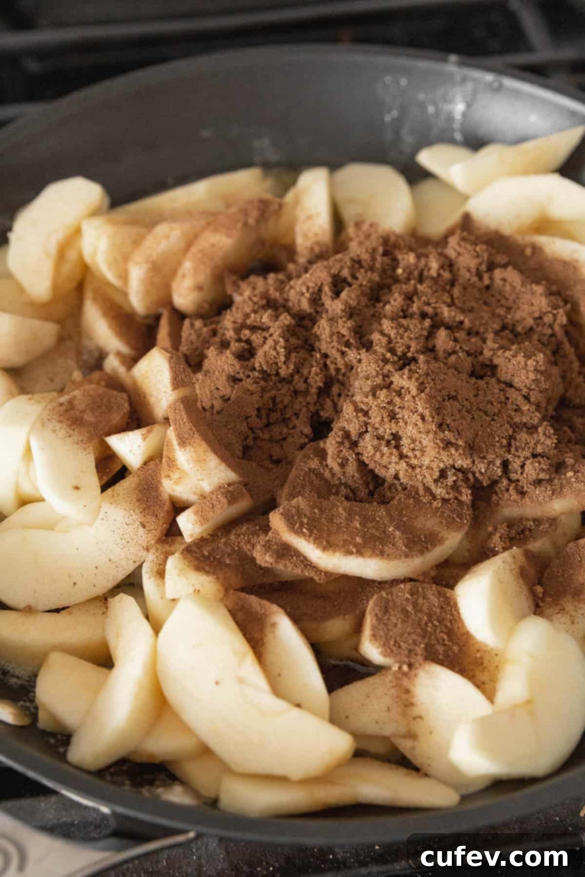 Cozy Vegan Bread Bake 8 Sliced apples, glistening with brown sugar and apple pie spice, gently cooking in a black nonstick pan on a stovetop.