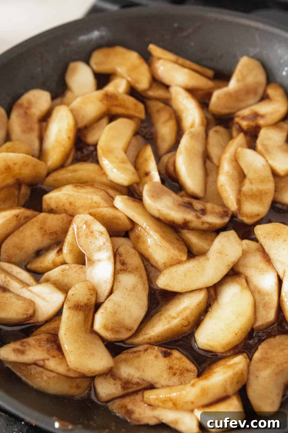 Cozy Vegan Bread Bake 9 Close-up of sliced apples evenly coated with apple pie spice and flour, cooking gently in a black pan.