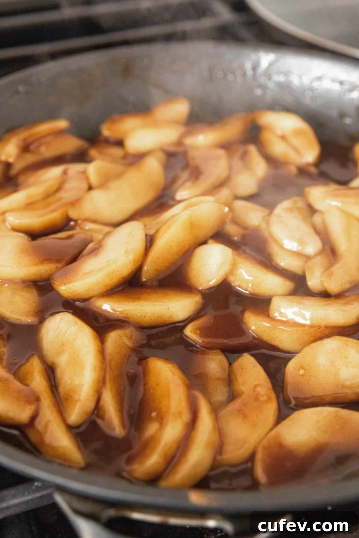 Cozy Vegan Bread Bake 10 A vibrant, steamy close-up of fragrant apple pie filling simmering in a pan, with tender apple slices coated in a glossy, spiced sauce.