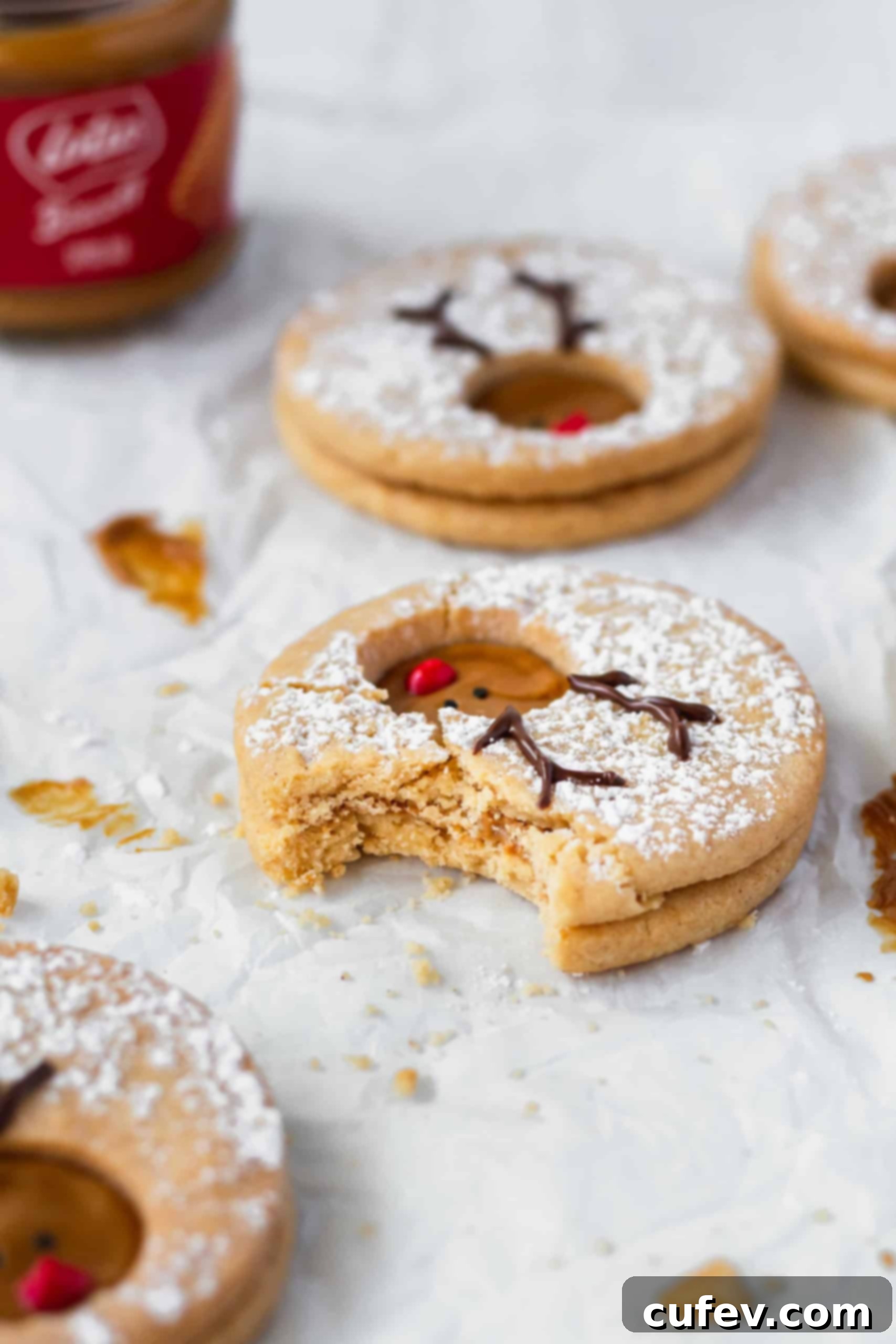 A close-up of a bitten Rudolph reindeer cookie on a white surface, revealing the delicious Biscoff filling.