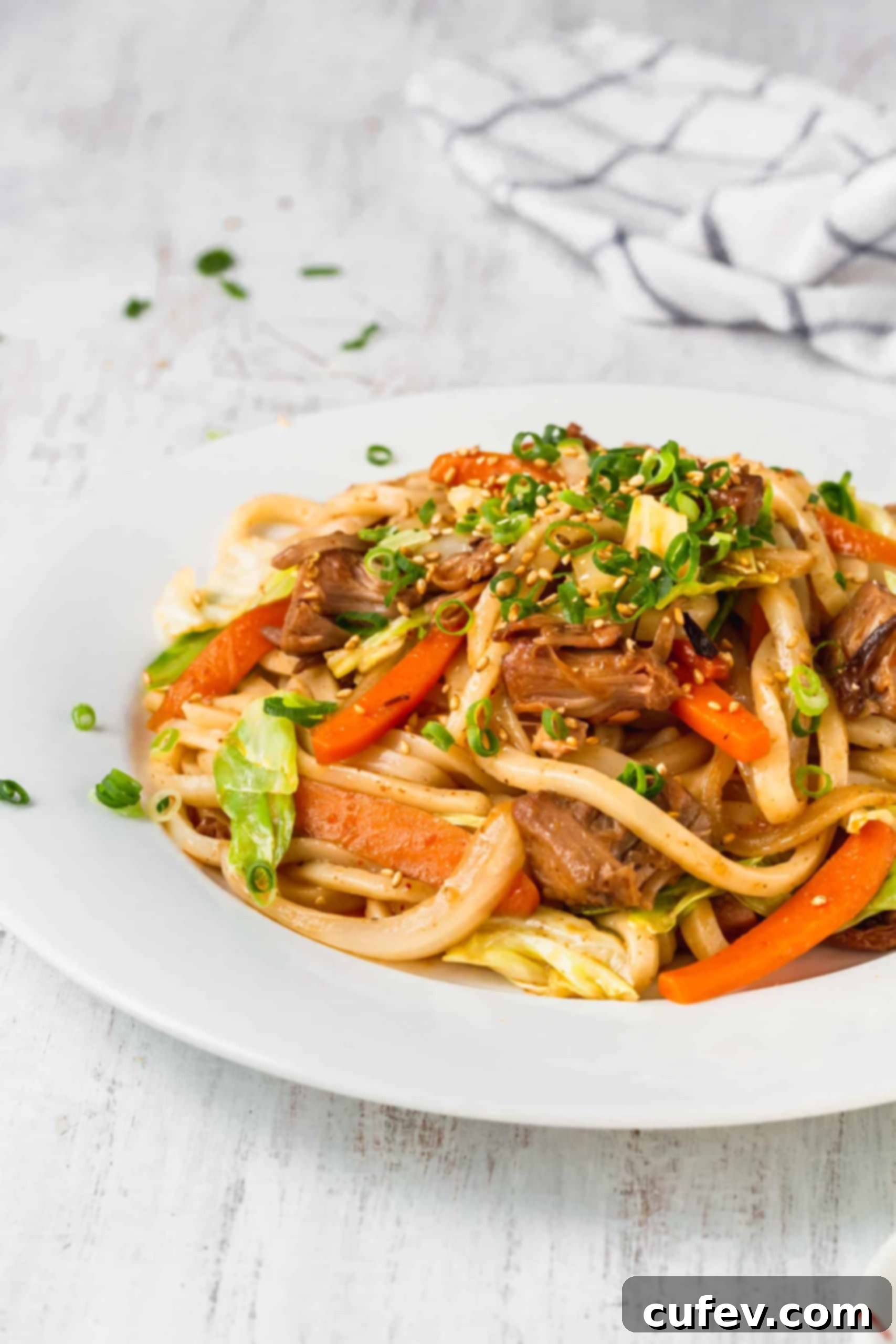A plate of vibrant vegan yaki udon, garnished with fresh green onions and sesame seeds, showcasing the rich sauce and noodles.