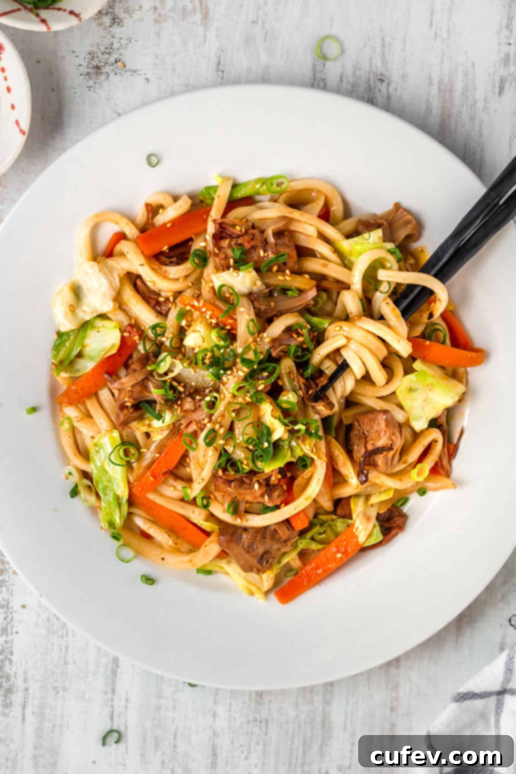 A close-up shot of spicy Massaman Yaki Udon noodles being lifted with black chopsticks, highlighting the texture and sauciness.