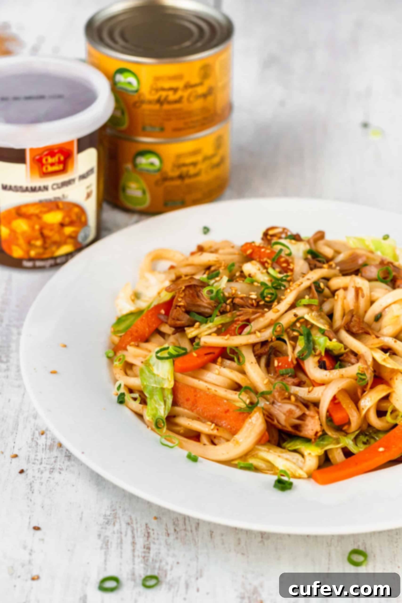 A close-up of a plate of spicy curry fried noodles, garnished with green onions and sesame seeds, ready for consumption.