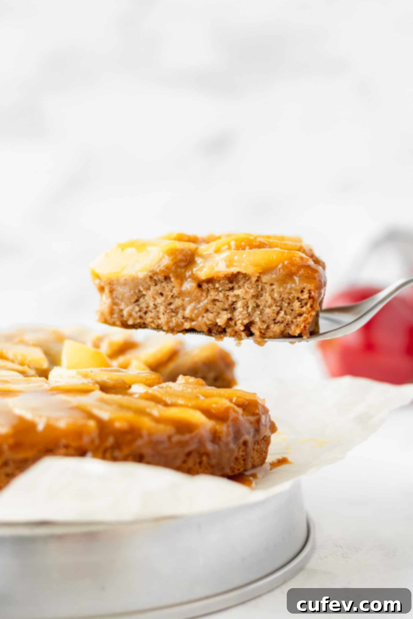 A beautiful slice of vegan apple cake being carefully lifted, showing layers of caramel, apples, and moist cake.