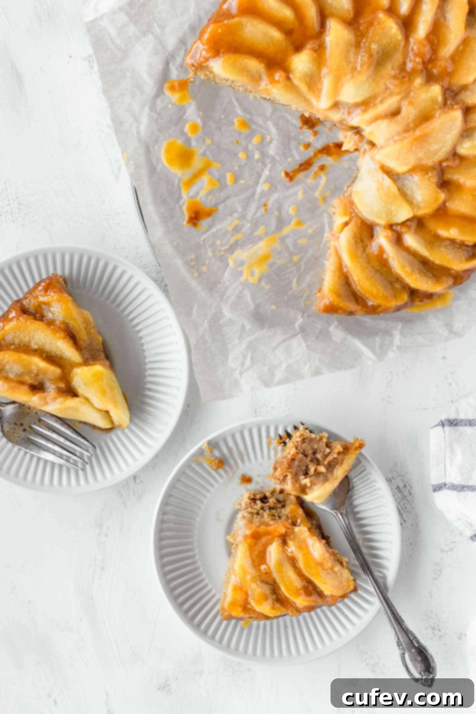 Two perfectly portioned slices of vegan apple cake on small white plates, with the remaining whole cake in the background.