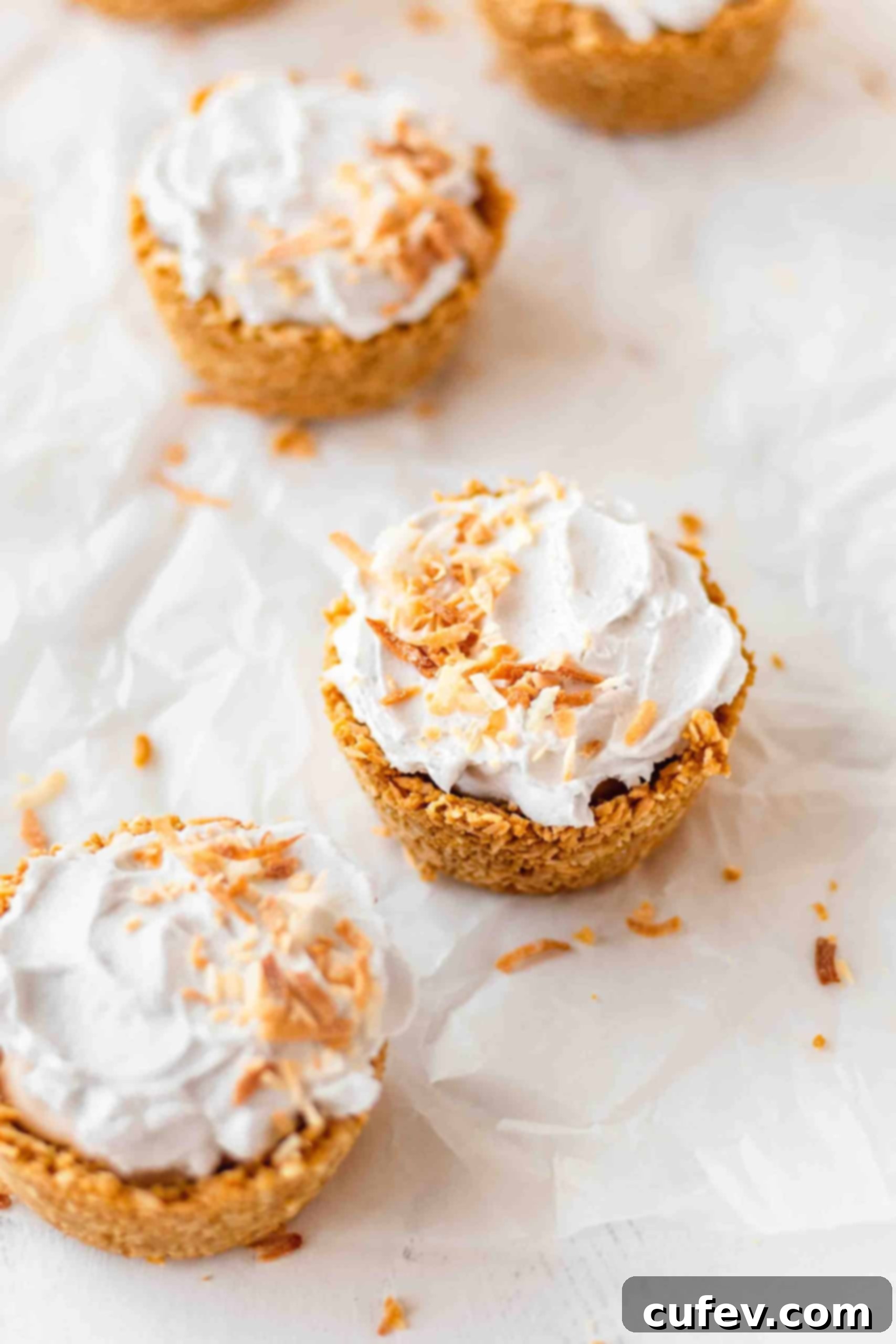 A tray of individual coconut cream pies resting on parchment paper, ready to be chilled