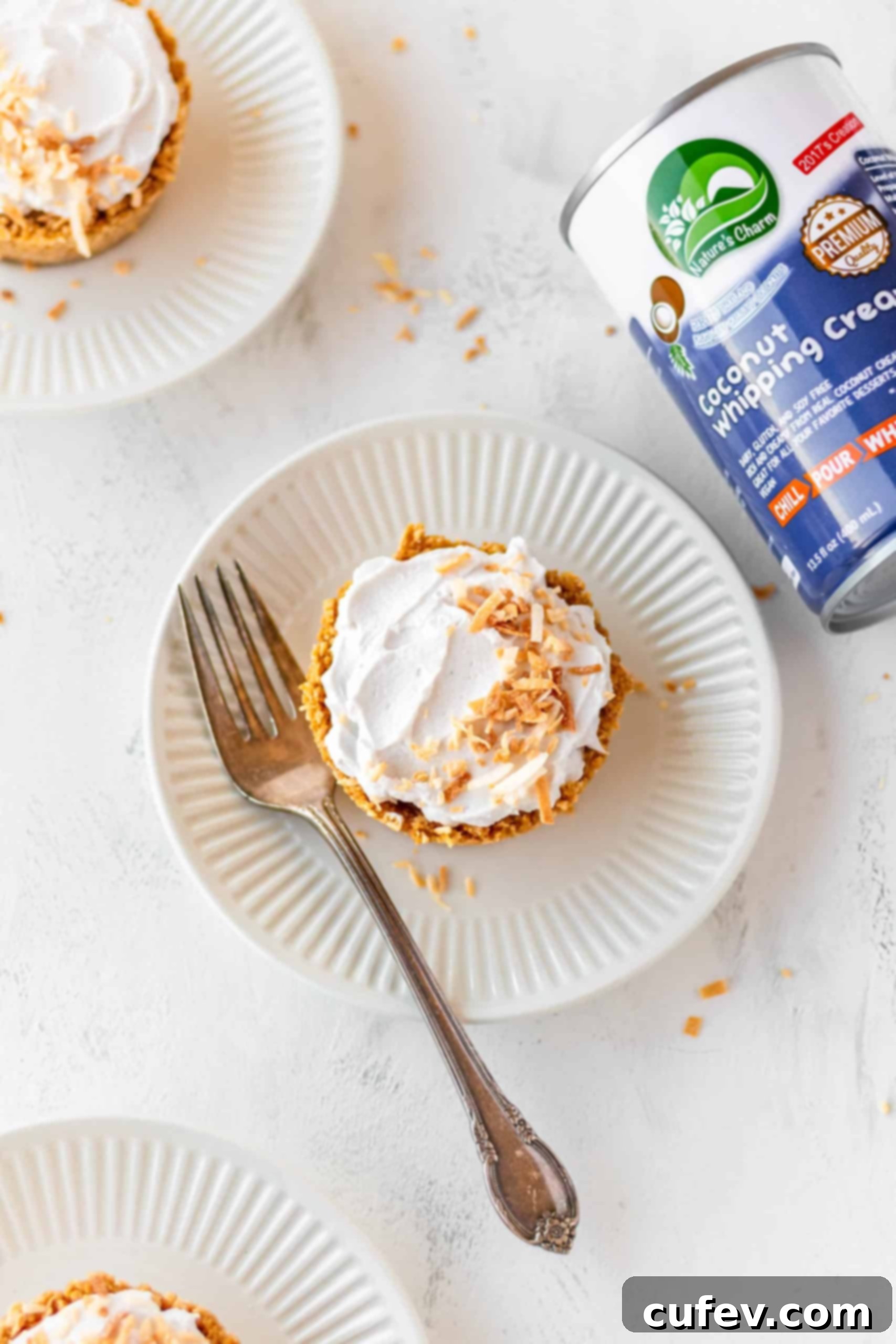 A single vegan coconut cream pie on a white plate, served with a fork, showing its distinct layers