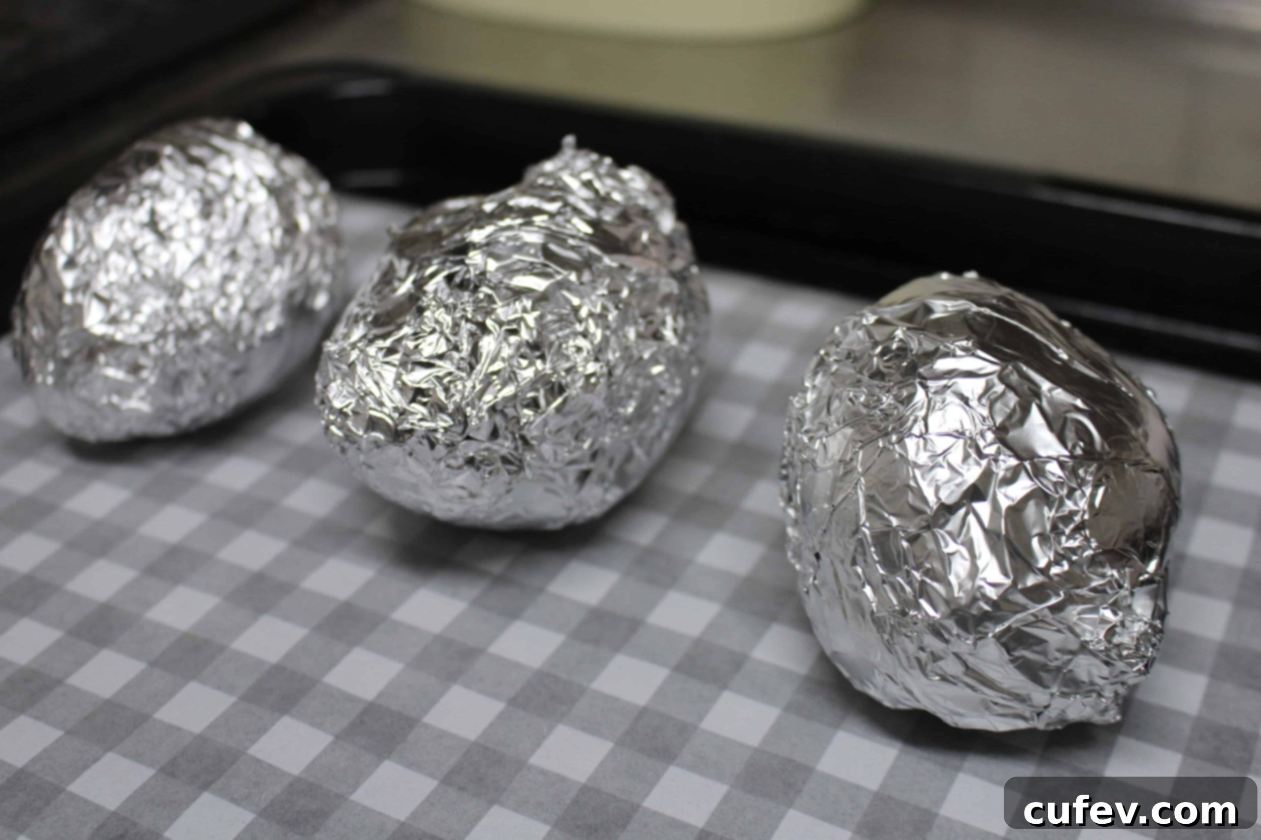 Japanese sweet potatoes individually wrapped in aluminum foil, ready for baking.