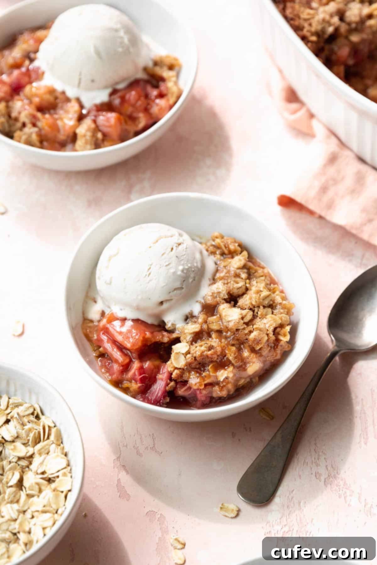 Rustic Rhubarb Crisp Gluten Free 2 Two bowls of vegan, gluten-free rhubarb crisp with vanilla ice cream next to the larger casserole dish filled with the rest of the dessert.
