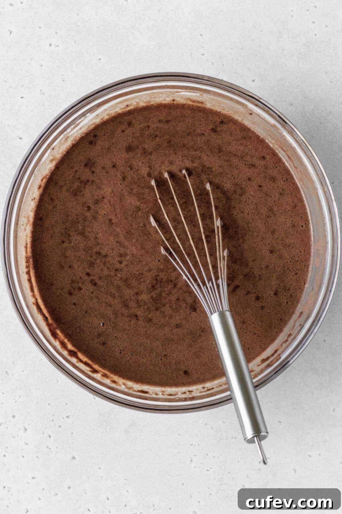Gluten-free German chocolate cake batter in a glass bowl with a whisk inside.