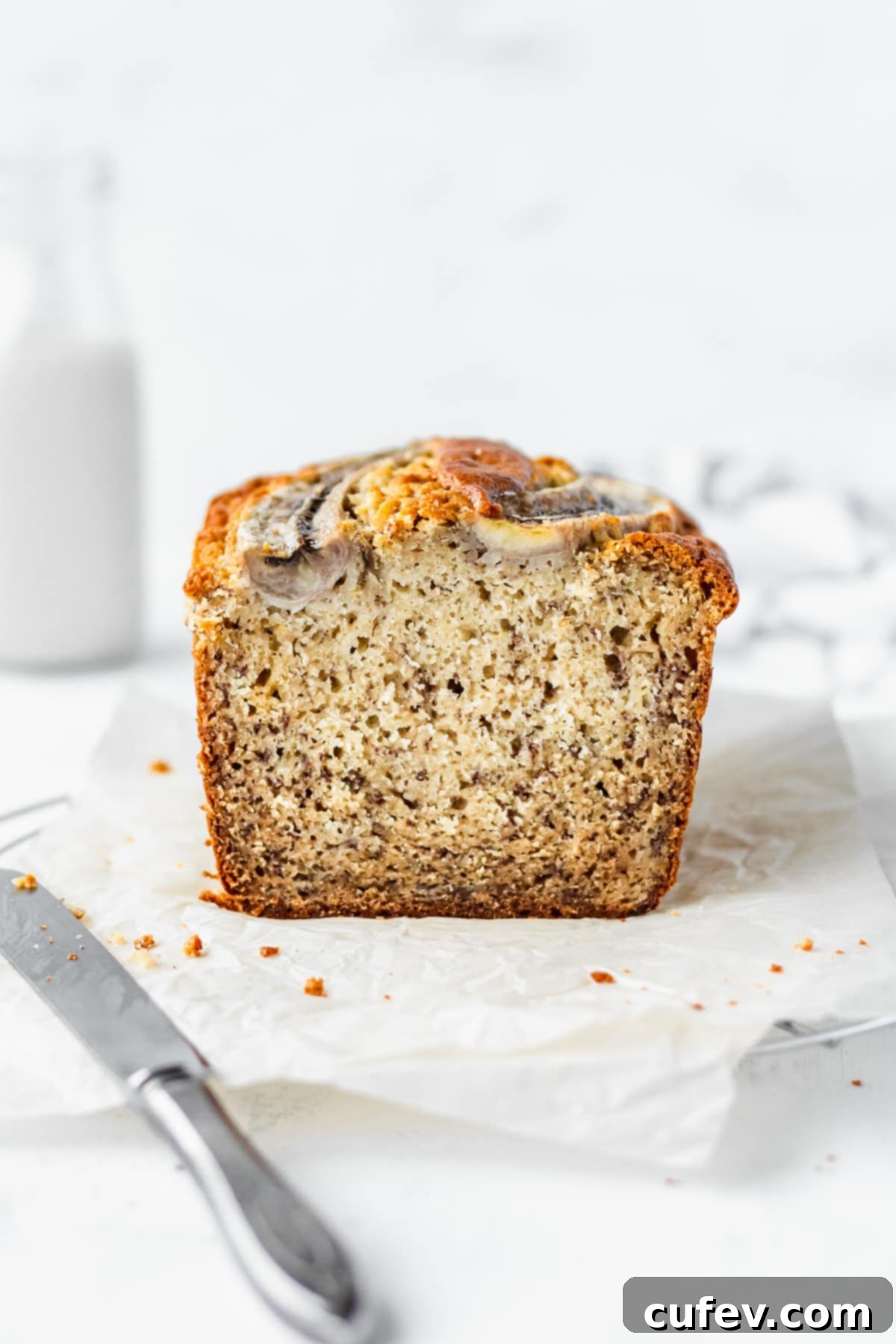 A perfectly sliced loaf of moist banana bread resting on a cutting board with a knife beside it, highlighting its tender crumb.