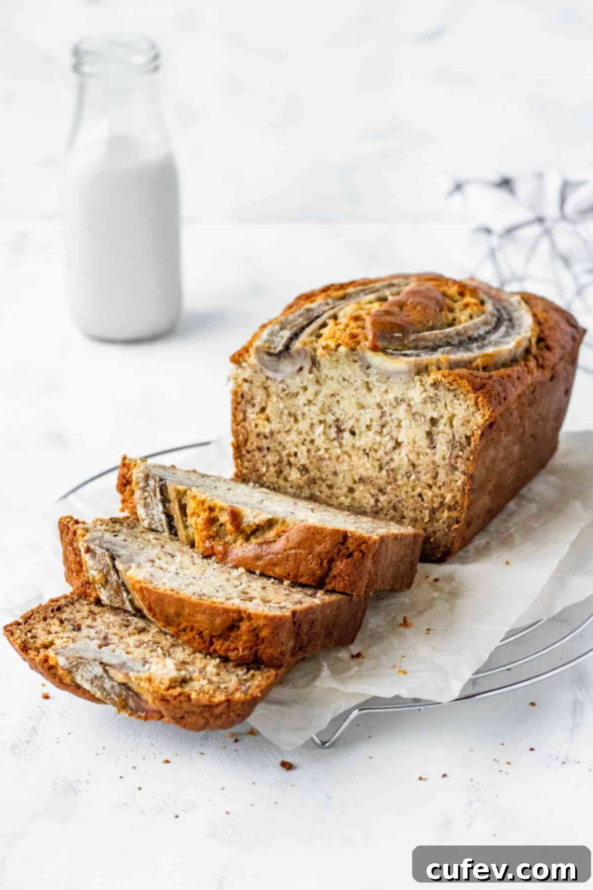 A freshly baked loaf of homemade banana bread cooling on parchment paper, with three inviting slices arranged in front.