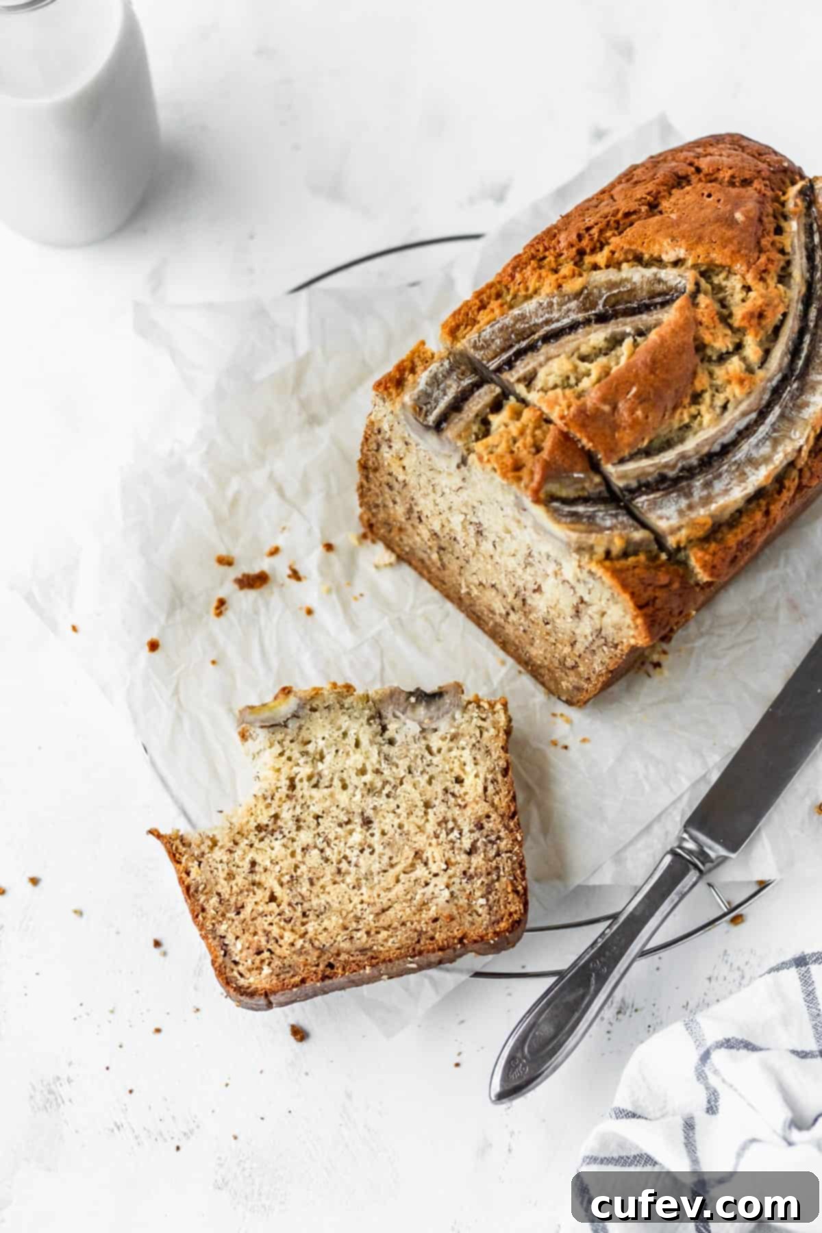 A delicious loaf of banana bread on parchment paper, with a slice already bitten into, showing its soft texture.