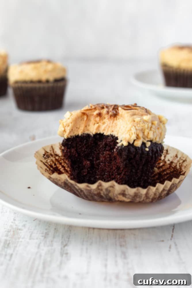 Close-up of a perfectly frosted chocolate peanut butter cupcake, garnished with chopped peanuts and a chocolate drizzle.