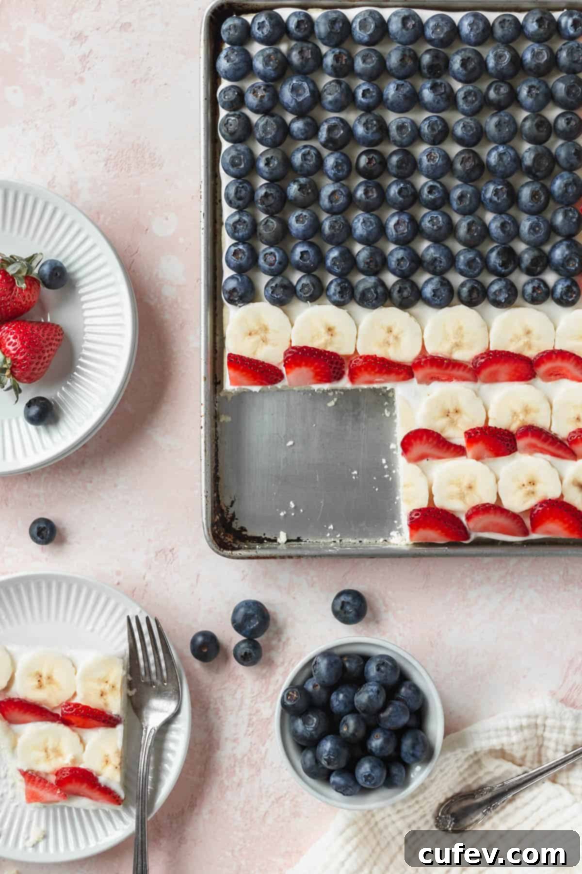 A delicious pan of patriotic American flag cookie cake, with one perfect slice carefully taken out, revealing the creamy frosting and colorful fruit layers beneath.