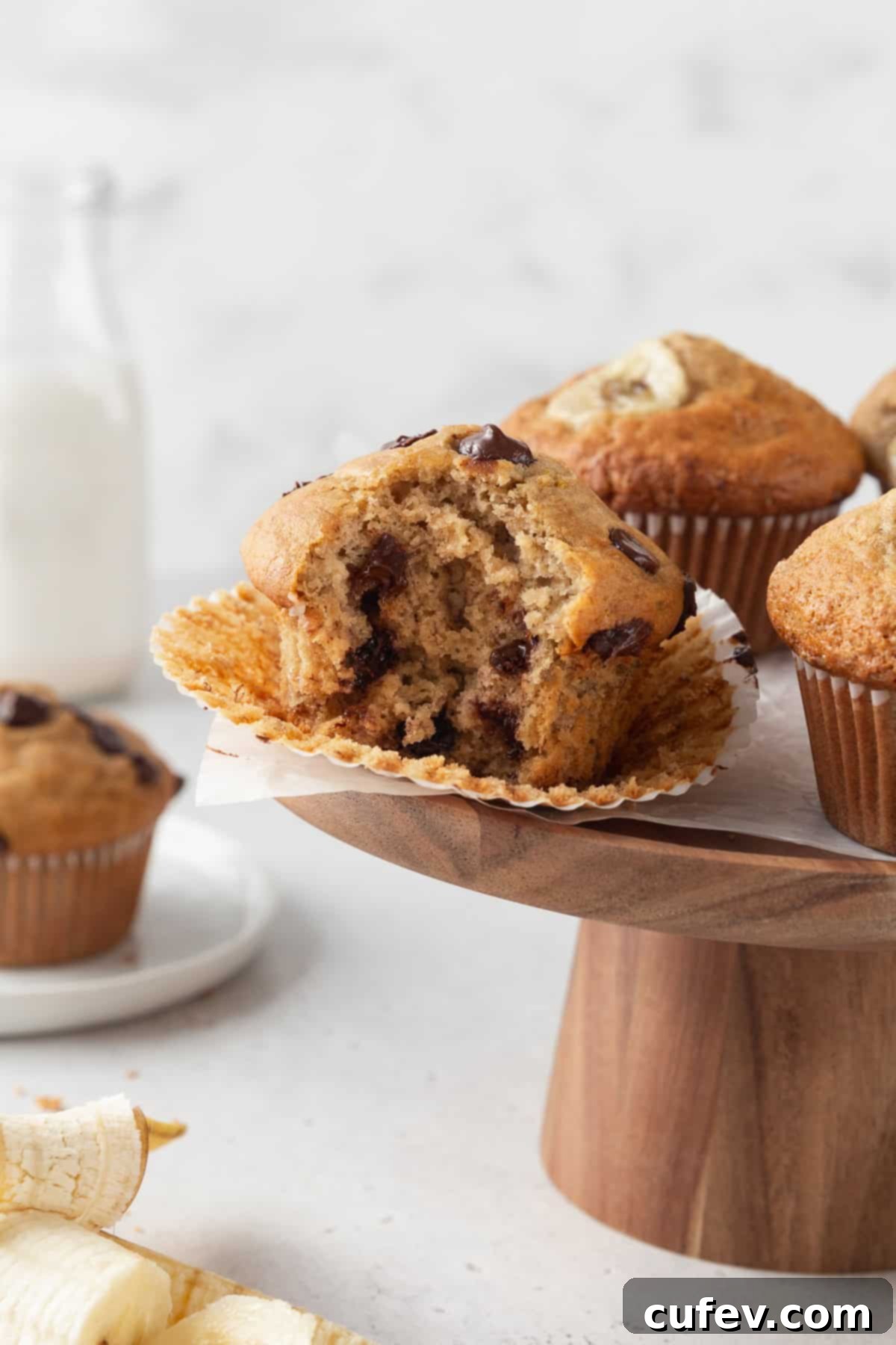 A perfectly baked gluten-free banana chocolate chip muffin with a bite taken out, resting on a wooden cake stand.