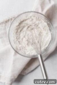 A glass bowl containing dry ingredients for muffins, ready to be mixed with a whisk.