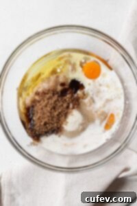 A glass bowl filled with wet ingredients for a muffin recipe, including mashed bananas and eggs.