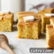 A piece of gluten-free cornbread with a pad of butter and drizzle of honey.