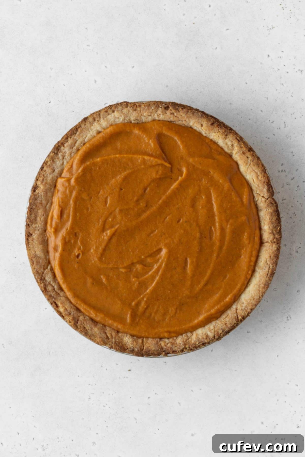 Unbaked dairy-free pumpkin pie with its rich orange filling nestled in a golden pie crust, waiting to be transformed in the oven.