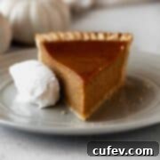 A slice of dairy-free pumpkin pie on a grey plate with a whipped coconut cream on the side, highlighting the dessert's appealing presentation.