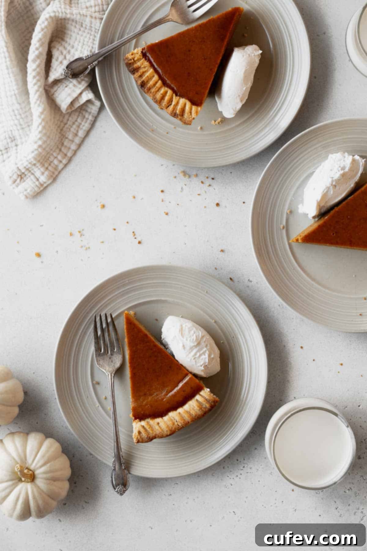 An inviting overhead arrangement of three slices of dairy-free pumpkin pie on distinct plates, each garnished with whipped cream and accompanied by a fork, ready for serving.