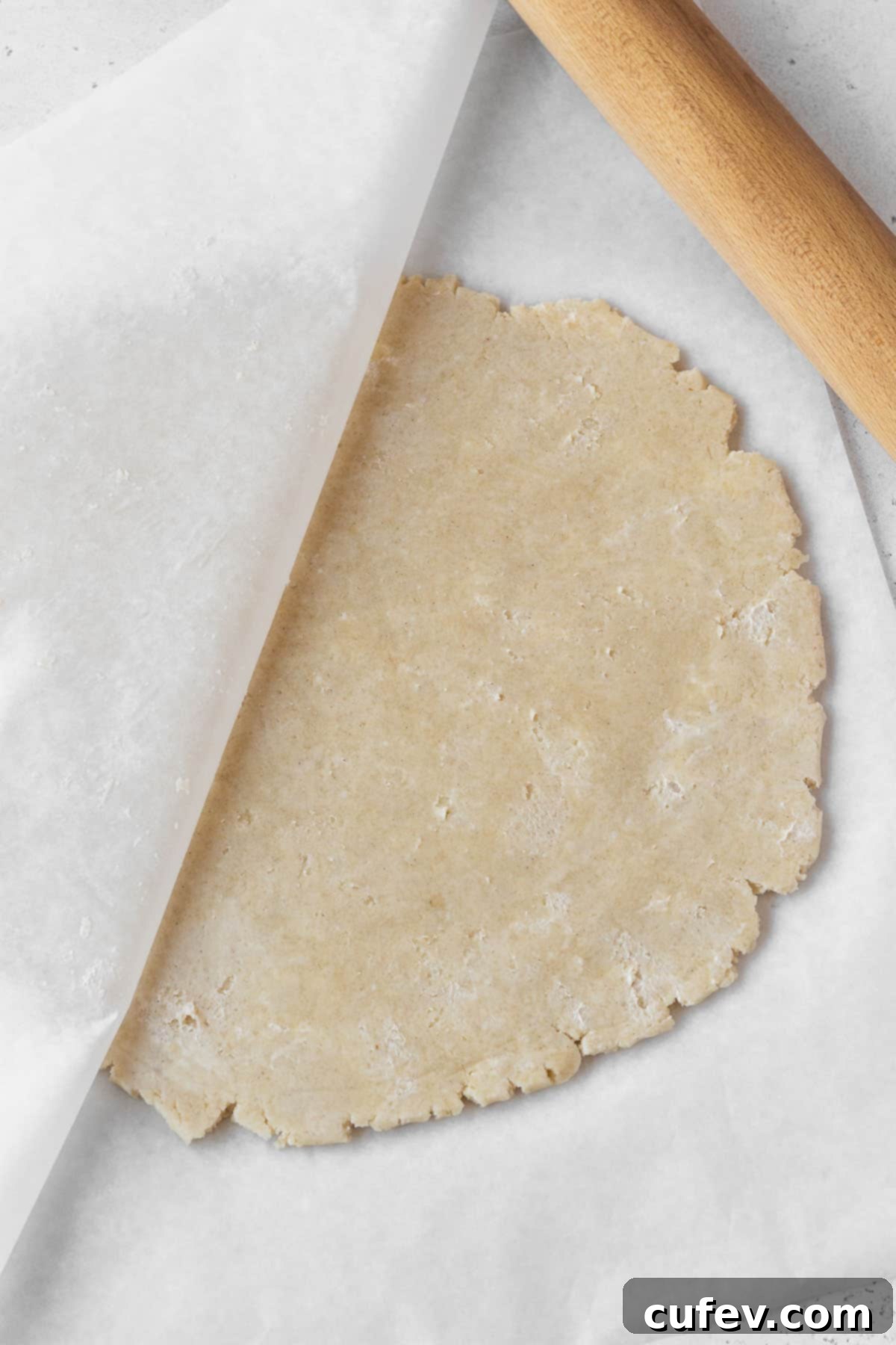 Dairy-free pie dough being skillfully rolled out between two sheets of parchment paper, a technique that prevents sticking and ensures an even thickness.