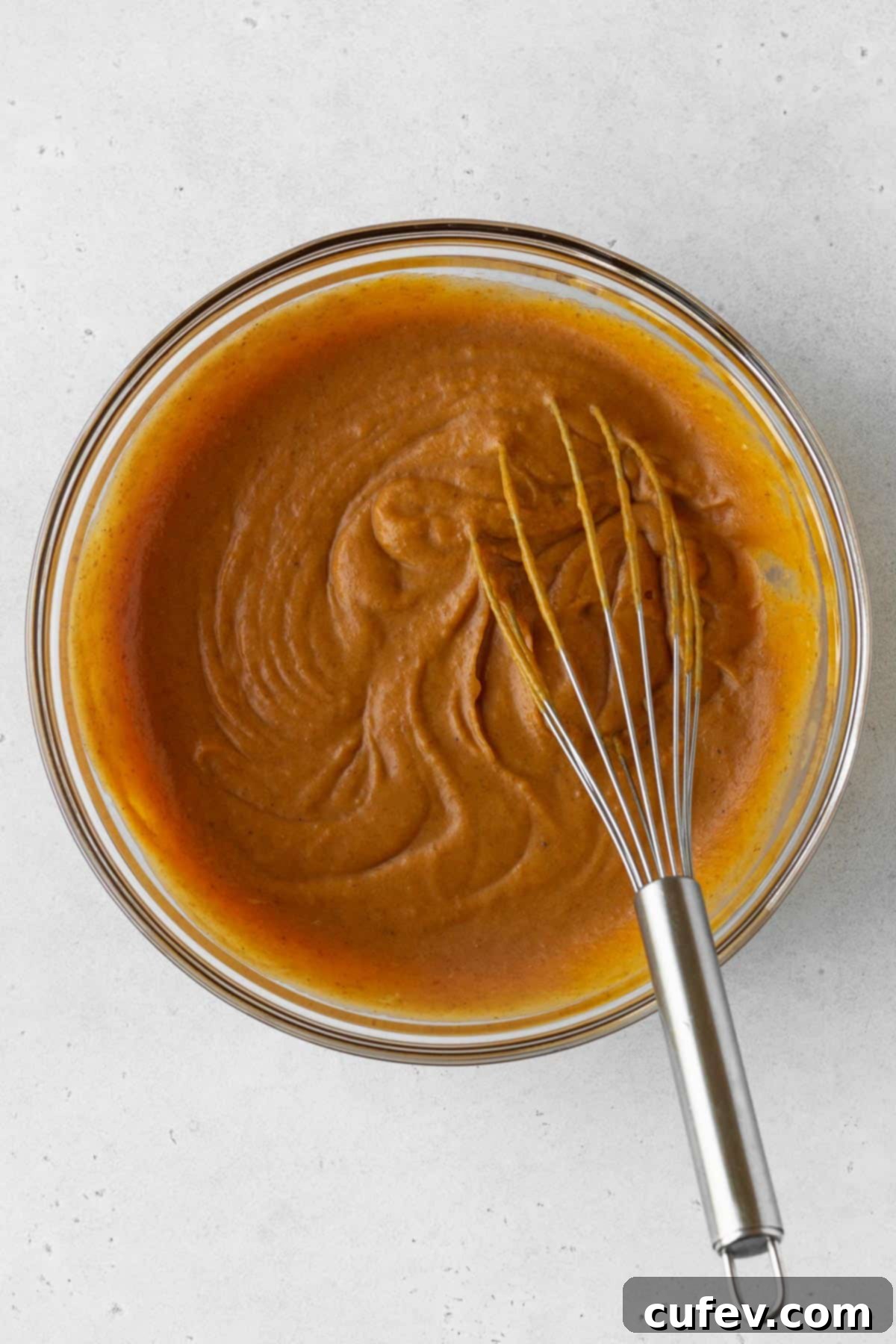All the dairy-free pumpkin pie filling ingredients expertly mixed together in a bowl using a whisk, showing a smooth and consistent orange mixture.