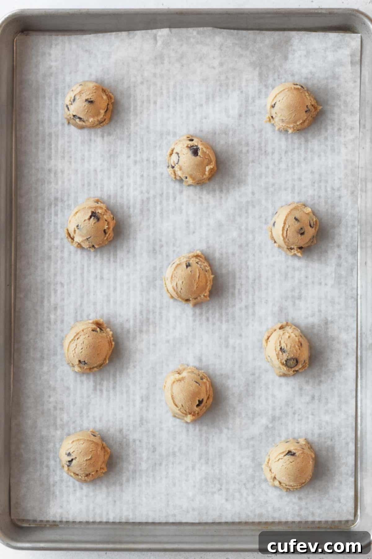 Balls of gluten-free chocolate chip cookie dough neatly arranged on a parchment-lined baking sheet, ready for the oven.