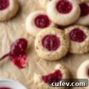 A square shot of gluten free thumbprint cookies next to a small spoon of jam on a brown parchment paper.