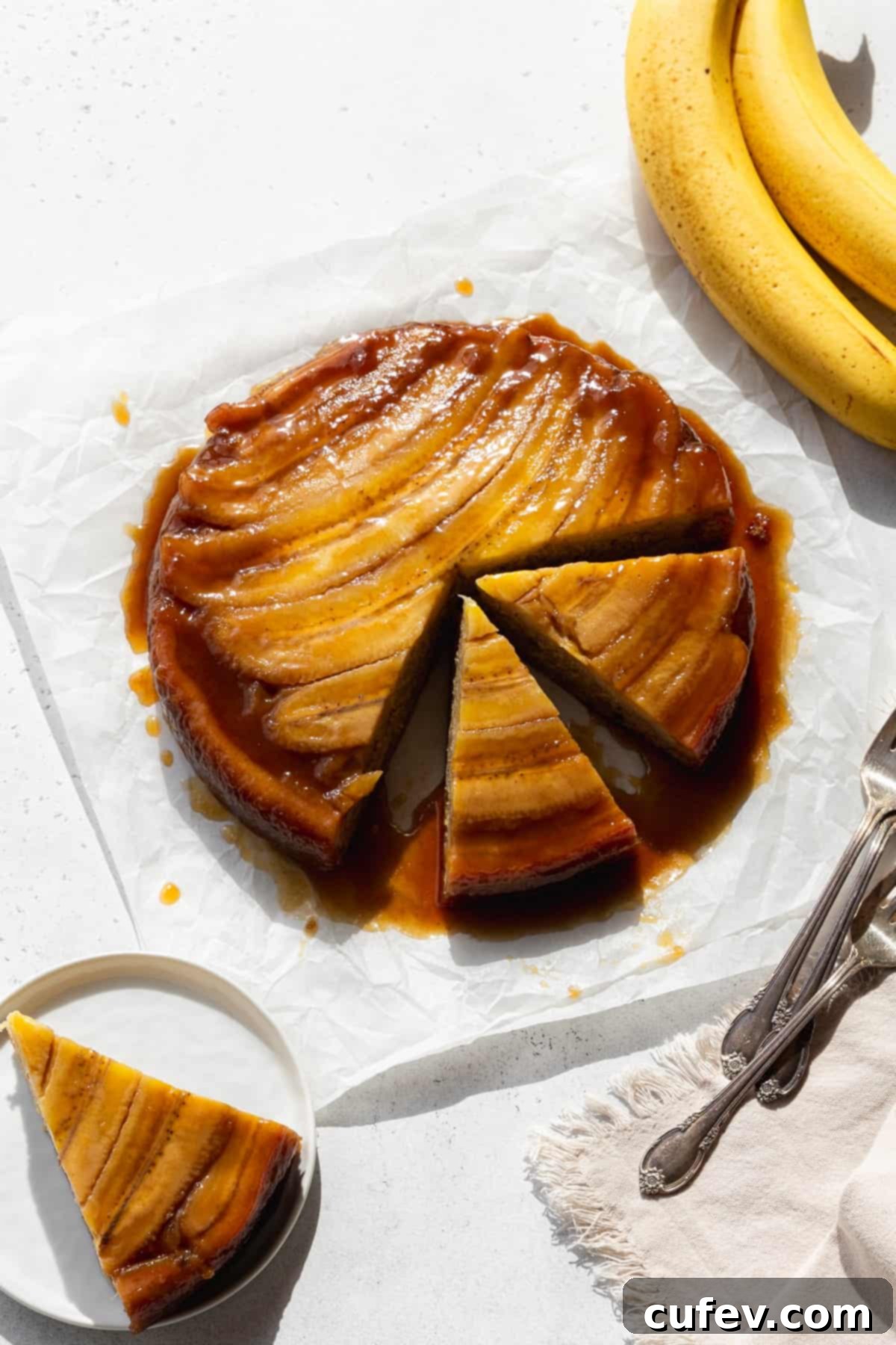 A banana upside down cake with two slices cut out, and another slice on a small dessert plate, showing the caramelized banana topping and moist cake.