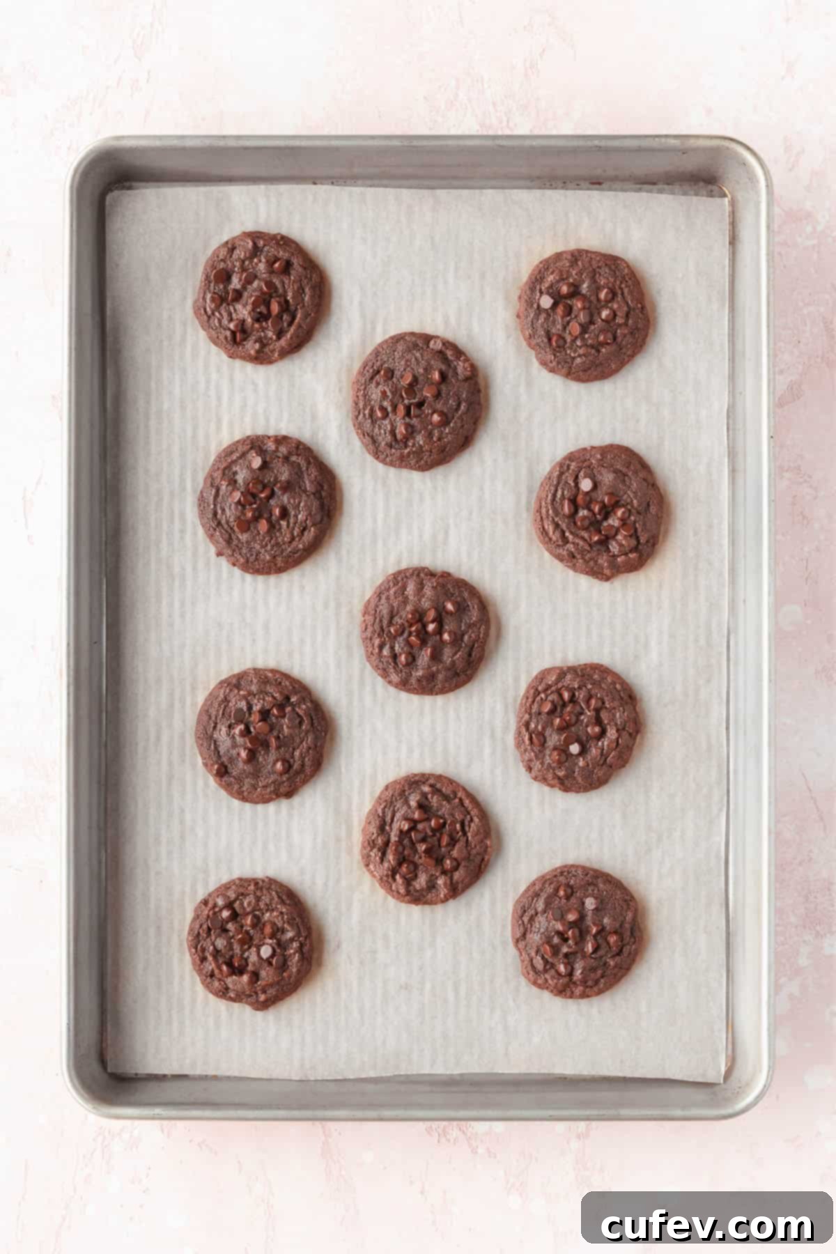 Freshly baked double chocolate cookies on a baking sheet immediately after coming out of the oven, showing soft centers and slightly set edges, ready for the shaping trick.