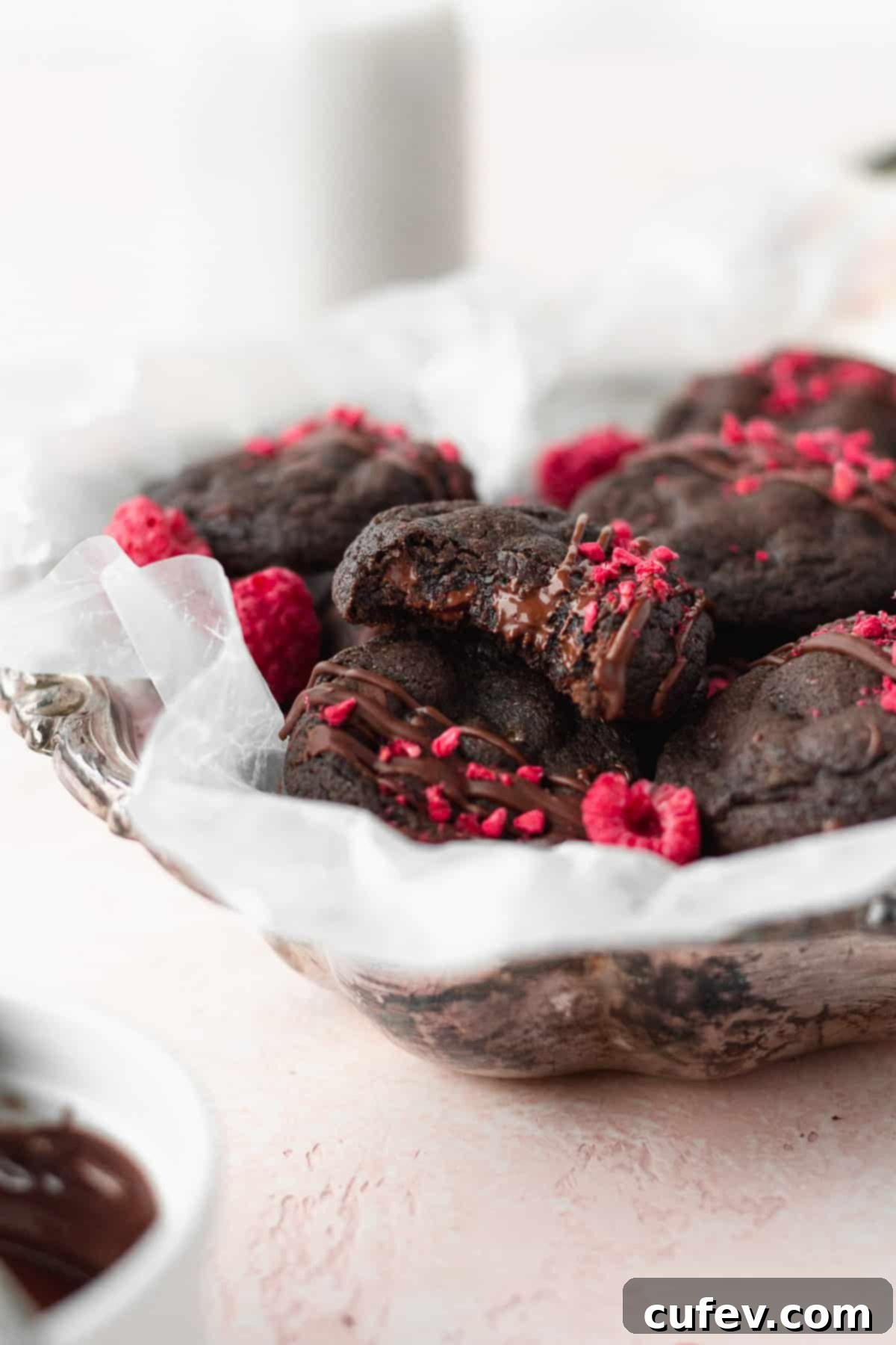 A silver dish filled with gluten-free double chocolate cookies, with one cookie bitten to reveal melted chocolate chips and its soft, fudgy interior.