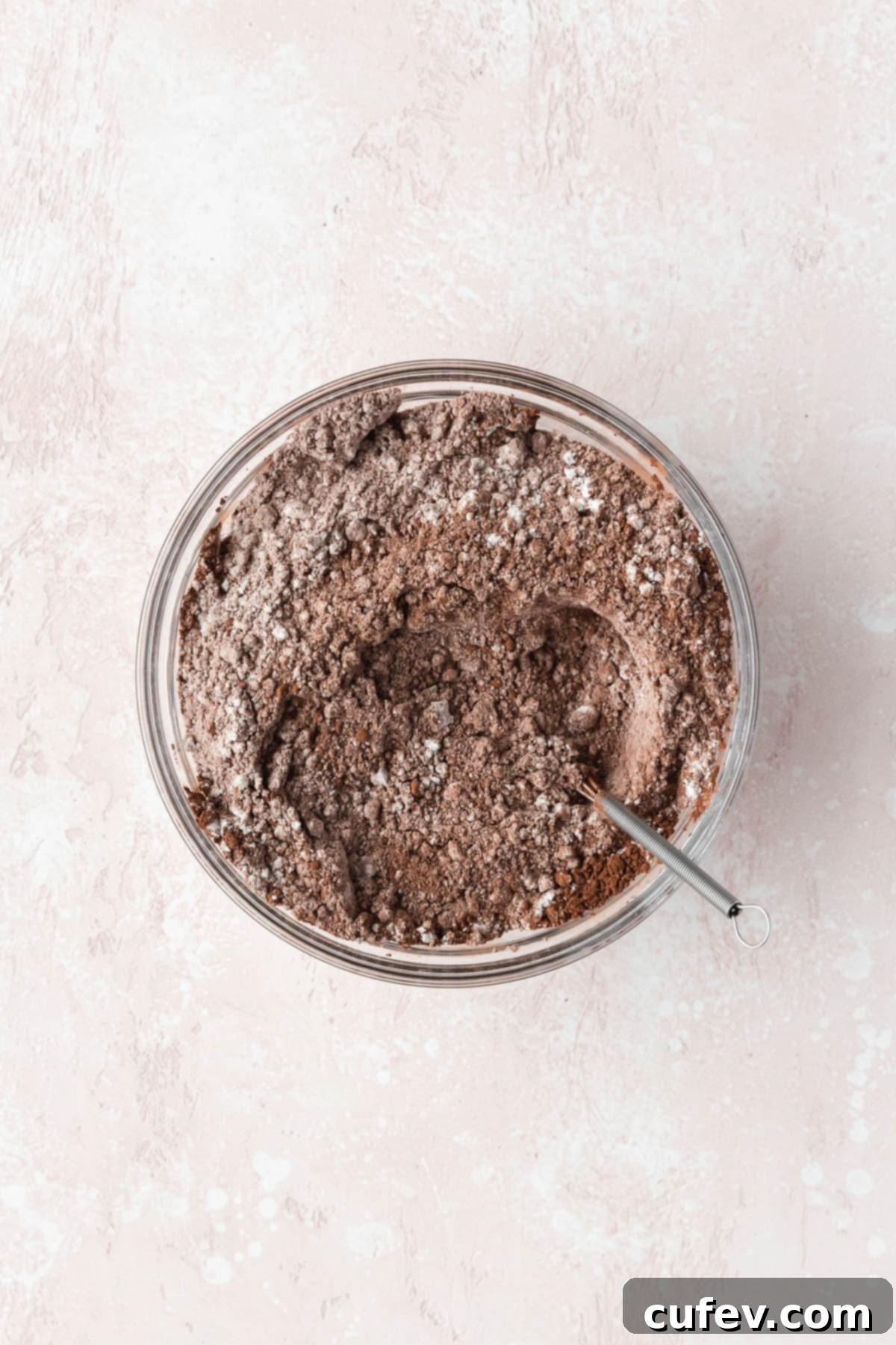 All-purpose flour, cocoa powder, salt, baking soda, and baking powder mixed together thoroughly in a glass bowl, creating a uniform dry mixture.