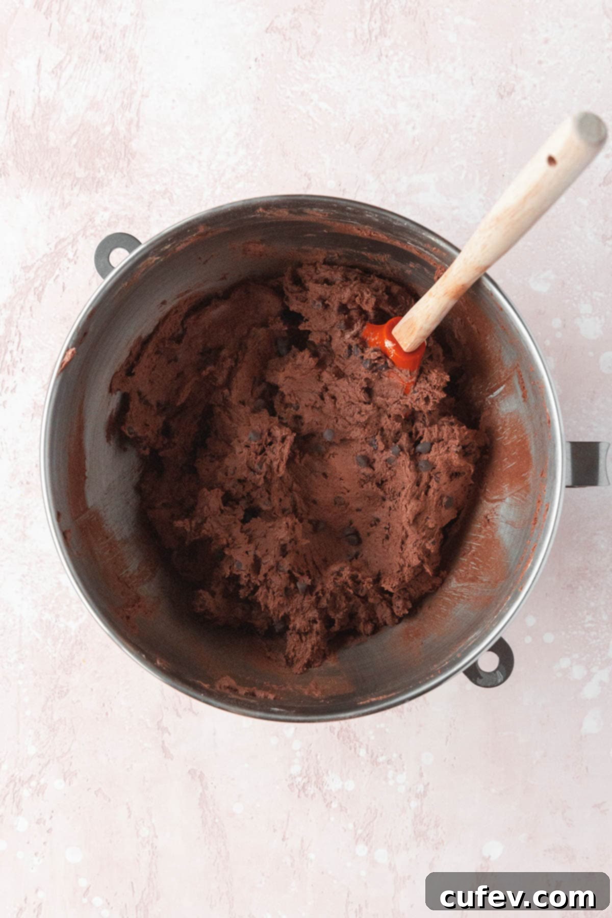 Chocolate chips being mixed into the dark chocolate cookie dough with a spatula, ensuring even distribution for every bite.