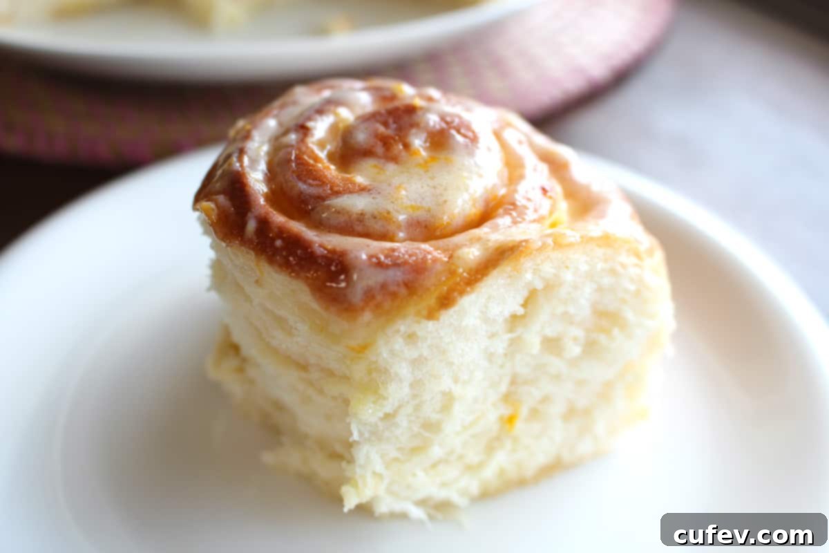 A fluffy, golden lemon roll generously topped with cream cheese frosting, presented on a white plate at a 45-degree angle.