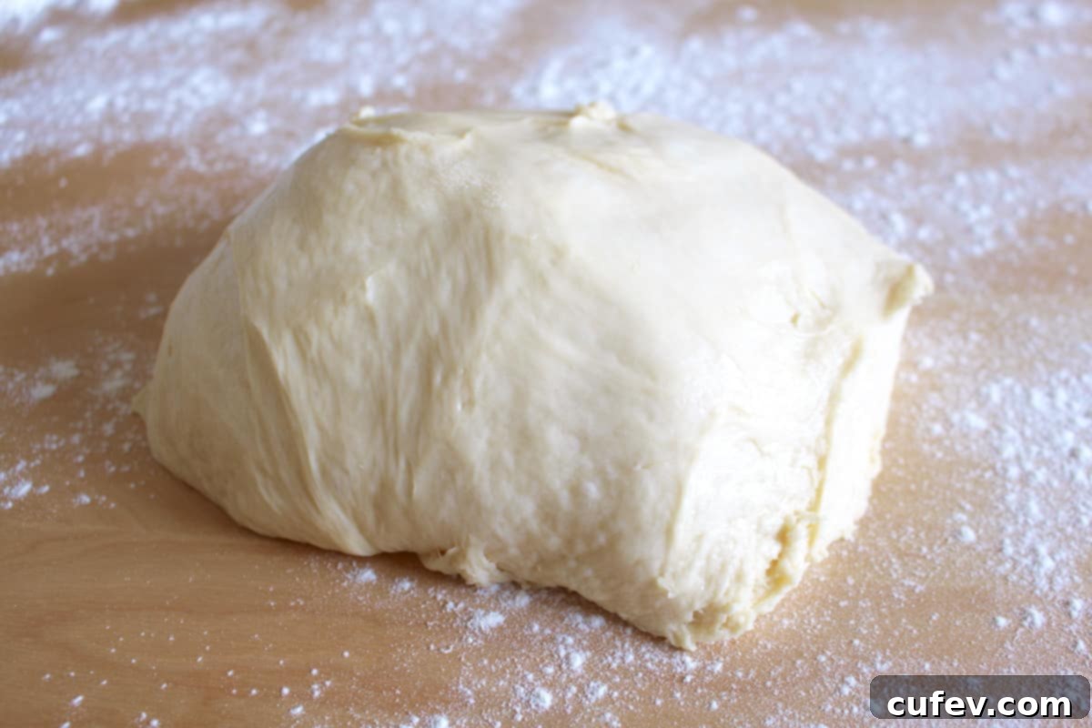 A perfectly kneaded ball of lemon cinnamon roll dough, dusted lightly with flour, resting on a wooden surface, ready for the next step.
